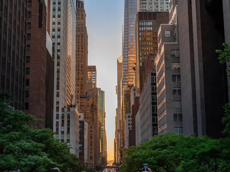 A city street between tall buildings at sunset, full of people taking photos